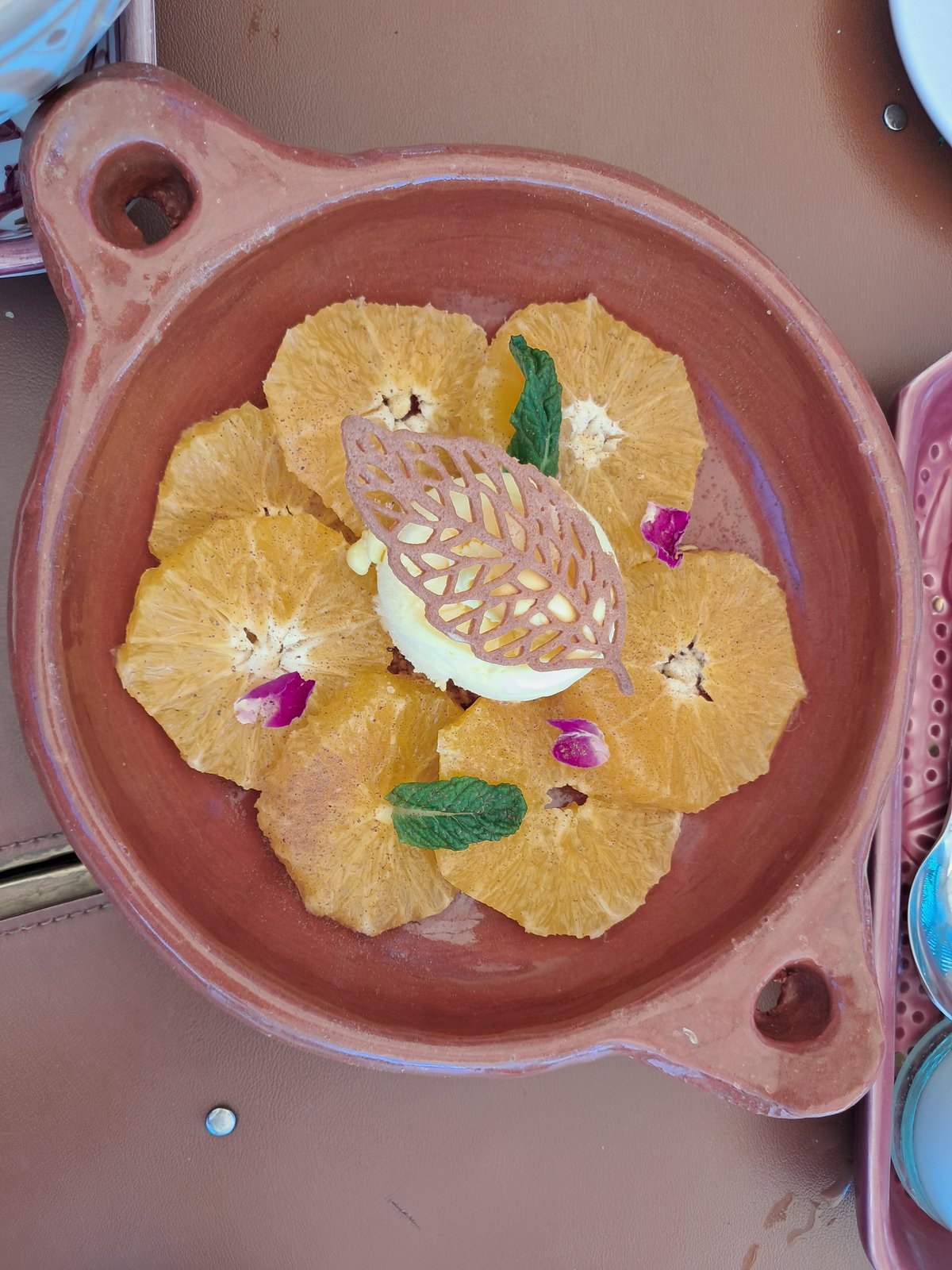A plate of sliced oranges with mint, rose petals and a chocolate leaf