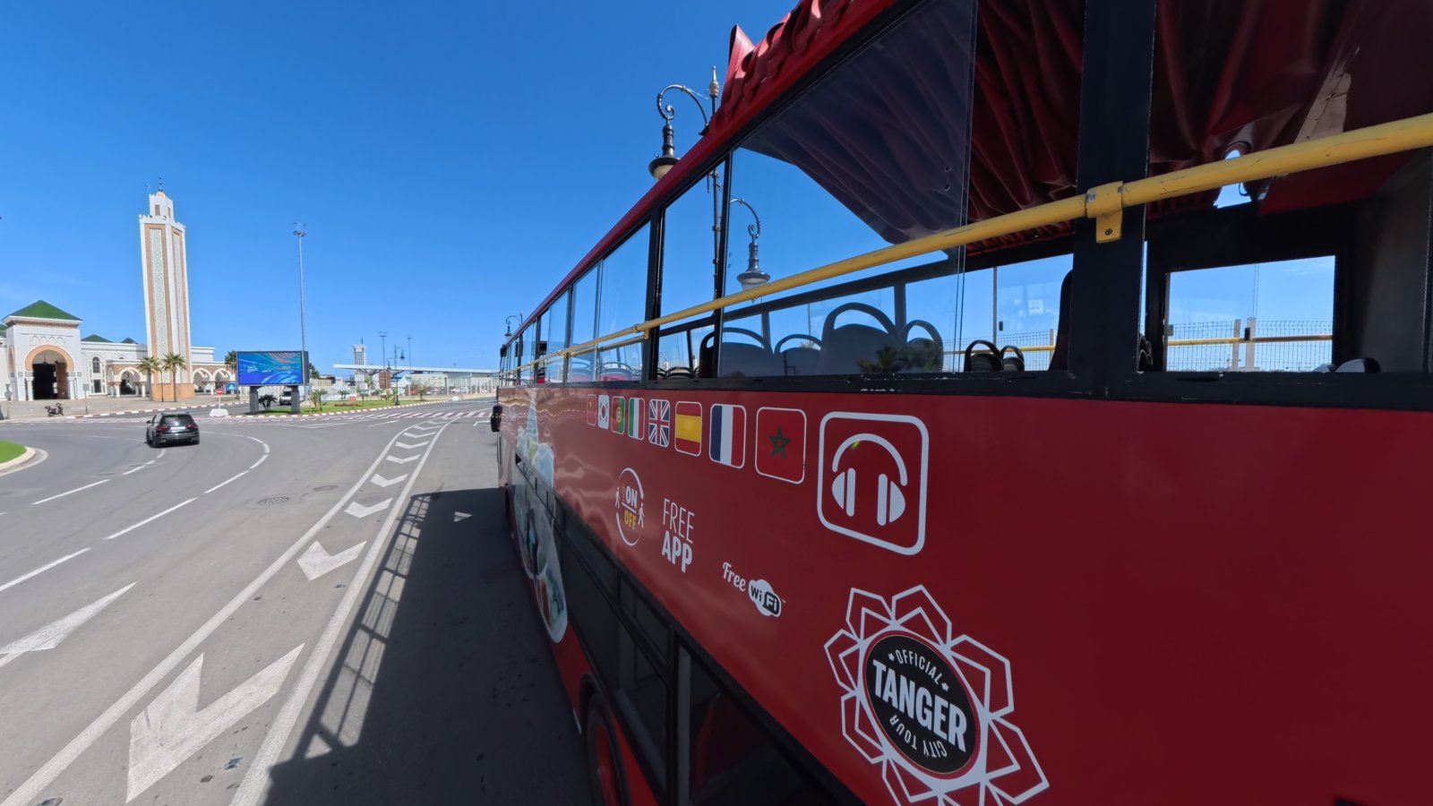 The official Tanger City Tour open-top bus beside a mosque